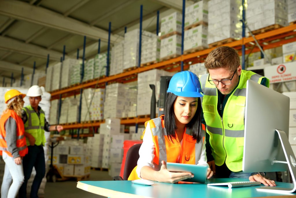 workers in warehouse at computer discussing supply chain management strategies
