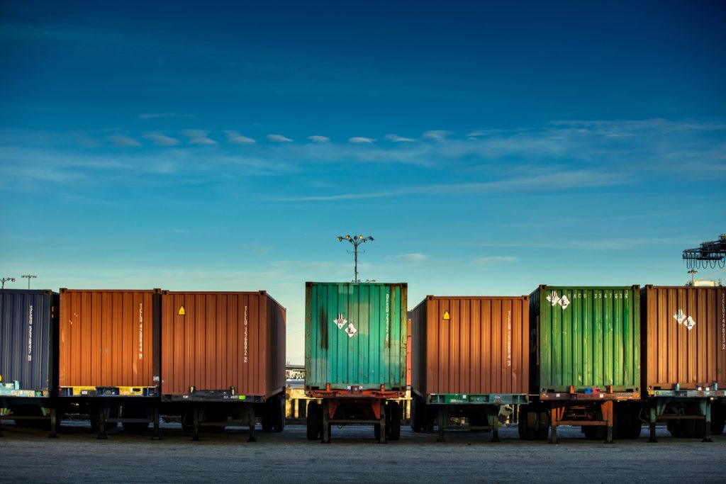 A rear view of a line of trucks loaded with shipping containers represents a part of a supply chain